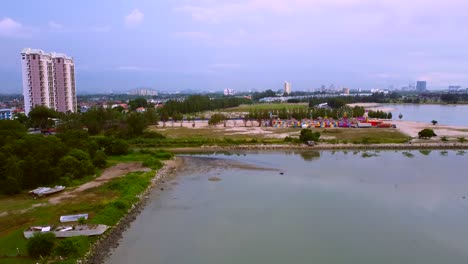 scenic view of amusement park near high rise buildings in malacca, malaysia surrounded by the calm lake water and lush green trees - aerial drone shot