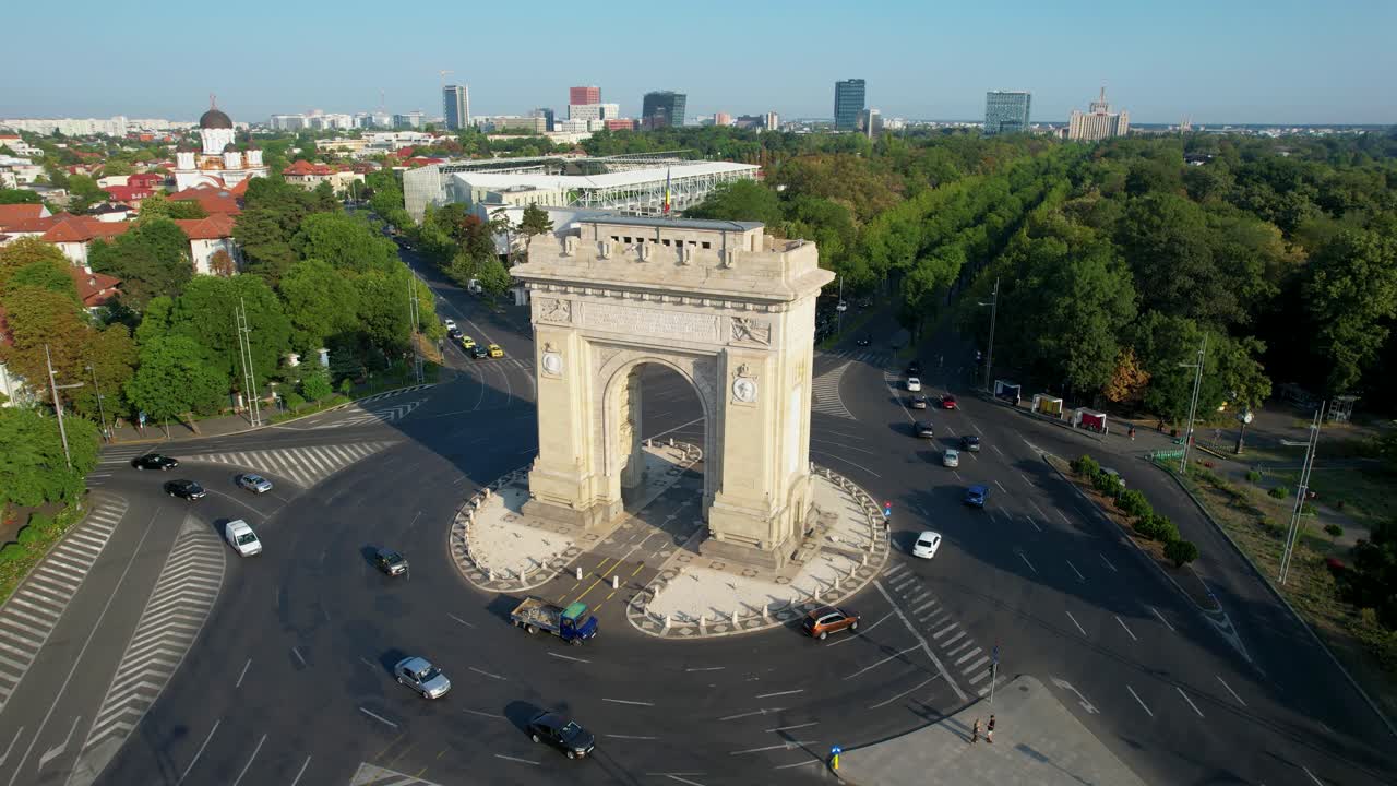 vista giratoria del arco del triunfo en bucarest, rumania, con imponentes edificios altos en el fondo, rodeado de vegetación exuberante con tráfico en movimiento por debajo