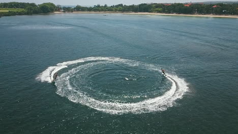 two young people on jetsurf boards doing doughnuts in the emerald green waters of bali, slow motion