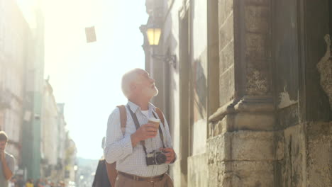 älterer tourist, der mit einer kamera und einem kaffee in einer hand geht