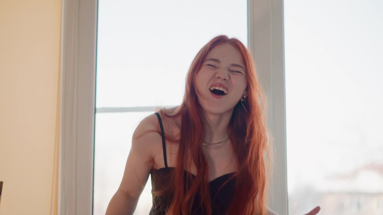 Mulher pensativa perto da janela. Cena matinal tranquila de mulher ruiva praticando letras. Um retrato íntimo de uma mulher ruiva contemplativa trabalhando nas letras de uma música sob a luz suave da manhã.