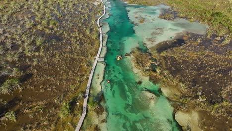 Aerial-view-tracking-people-in-a-inflatable-kayak,-paddling-through-the-narrow-channel-of-the-Rapidos-de-Bacalar-,-in-sunny-Mexico