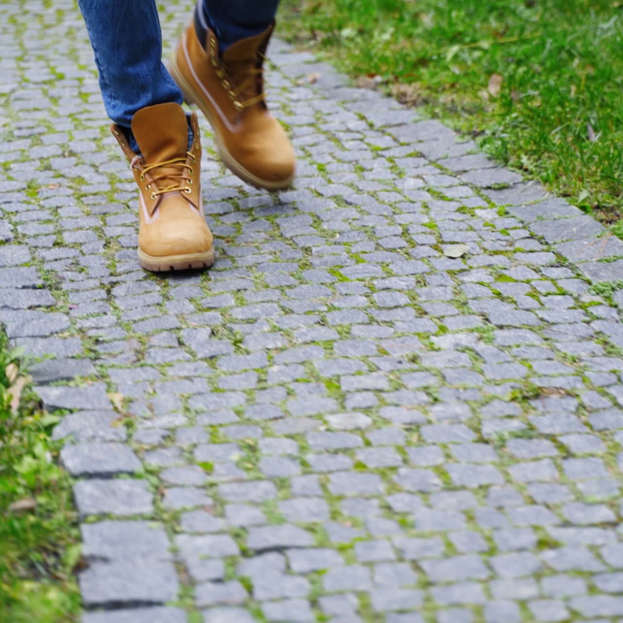 Stylish man's legs outdoors. Male in brown boots walking a stone path. Man's feet wearing jeans and shoes walks on terrace in autumn time. Close-up.