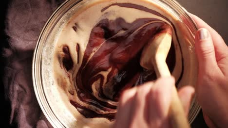 topview of stirring chocolate drops, cream and butter with wooden spoon