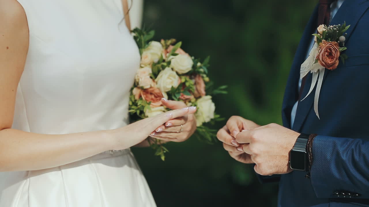 Newlyweds exchange rings at the wedding ceremony over green grass background. Wedding rings.