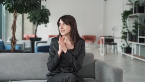 young,-beautiful-woman-in-a-suit-cheerfully-talks-and-gestures-with-her-hands-while-sitting-on-the-couch