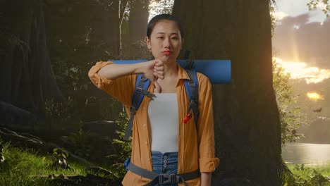 asian female hiker with mountaineering backpack showing thumbs down gesture while exploring forest nature