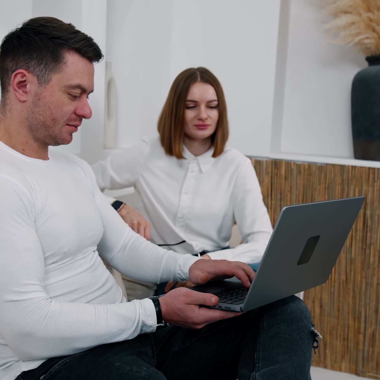 Uomo muscoloso e attraente tiene il computer portatile parlando con una donna seduta accanto. La donna sorride e fa un gesto di approvazione.