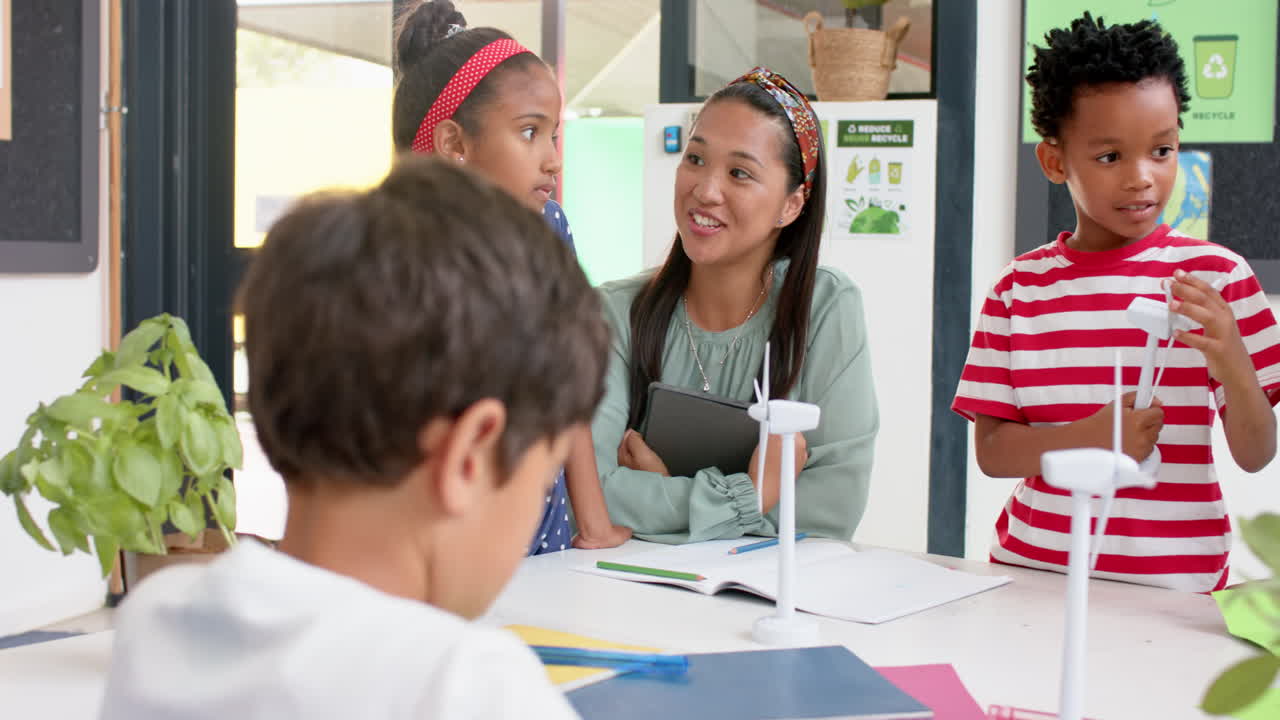 In school, teacher with tablet engaging with students working on wind turbine models
