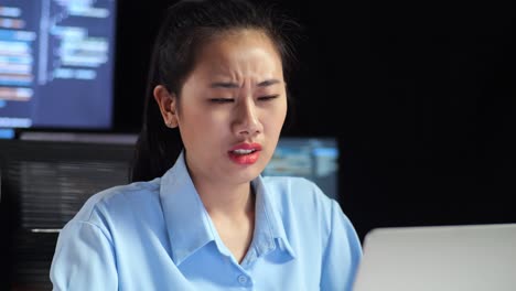 close up of asian female programmer having a headache while writing code by a laptop using multiple monitors showing database on terminal window desktops in the office