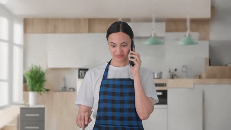 happy indian housewife talking on call while making food