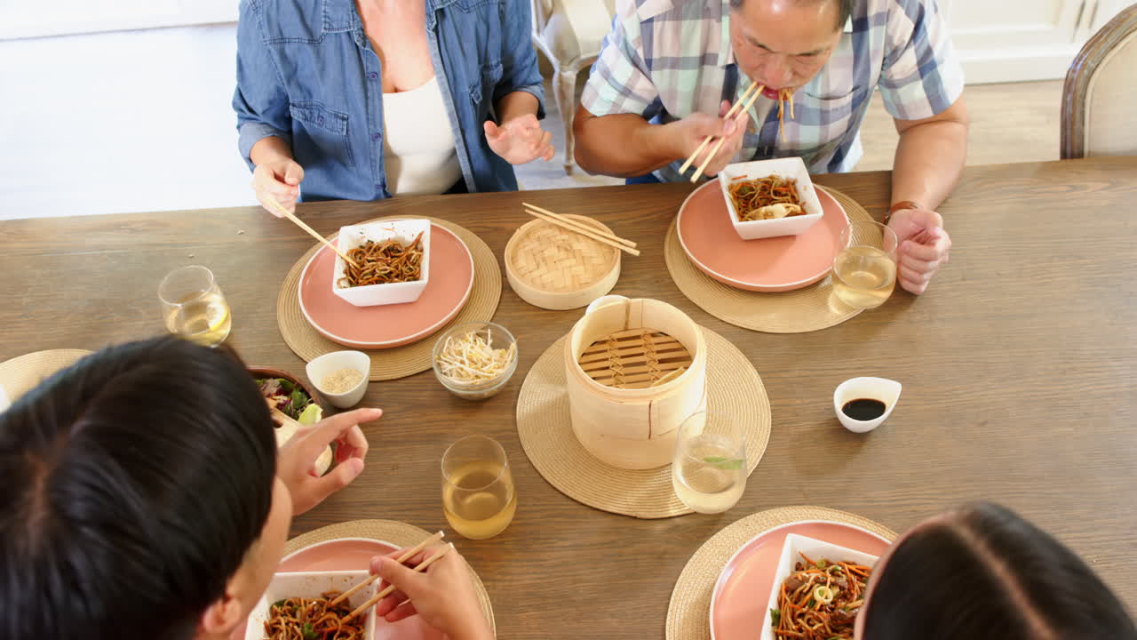 Eating noodles with chopsticks, family enjoying meal together at dining table
