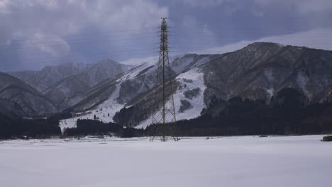 contra el dramático paisaje invernal de hakuba, japón, una captura cautivadora revela un pilar eléctrico en medio de los cielos nublados, mientras dos coches atraviesan elegantemente el terreno cubierto de nieve