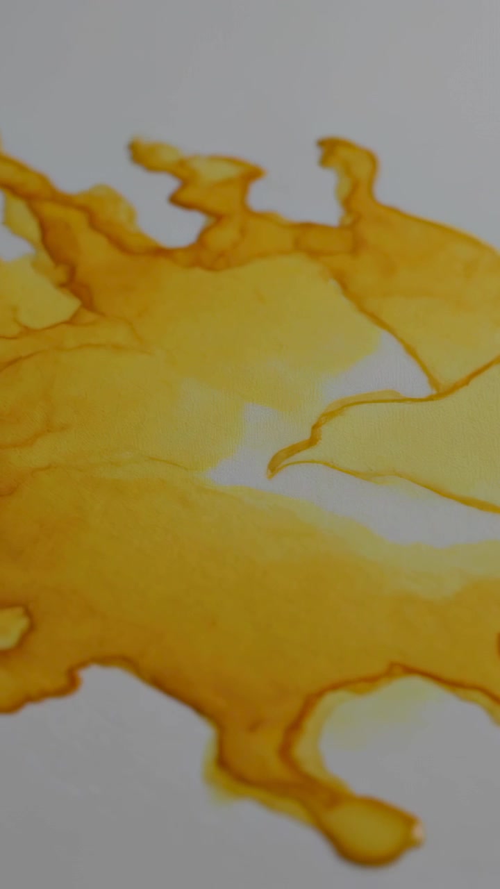 Video vertical: Depositando gotas, líquido amarillo anaranjado extendiéndose sobre una sábana blanca, creando filamentos.