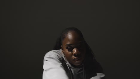 studio portrait shot of young woman wearing hoodie dancing with low key lighting against grey background 12