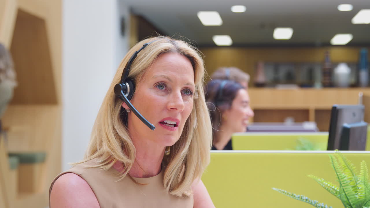 Volwassen zakenvrouw met telefoonheadset die spreekt met een beller in een klantenservicecentrum