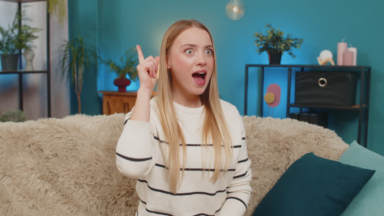 Caucasian woman eureka moment on sofa thinking problem solution smiling raising finger indoors idea