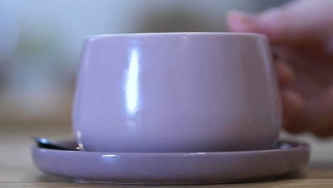 Customer-picking-up-coffee-cup-from-saucer-in-cafe,-closeup-side-angle