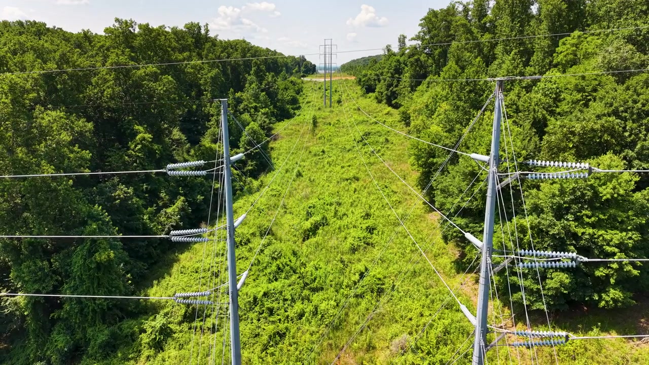 High-voltage transmission corridor near Chattanooga, Tennessee, United States, revealing steel monopoles, overhead conductors, cleared utility easement and deciduous woodland, drone pullback.