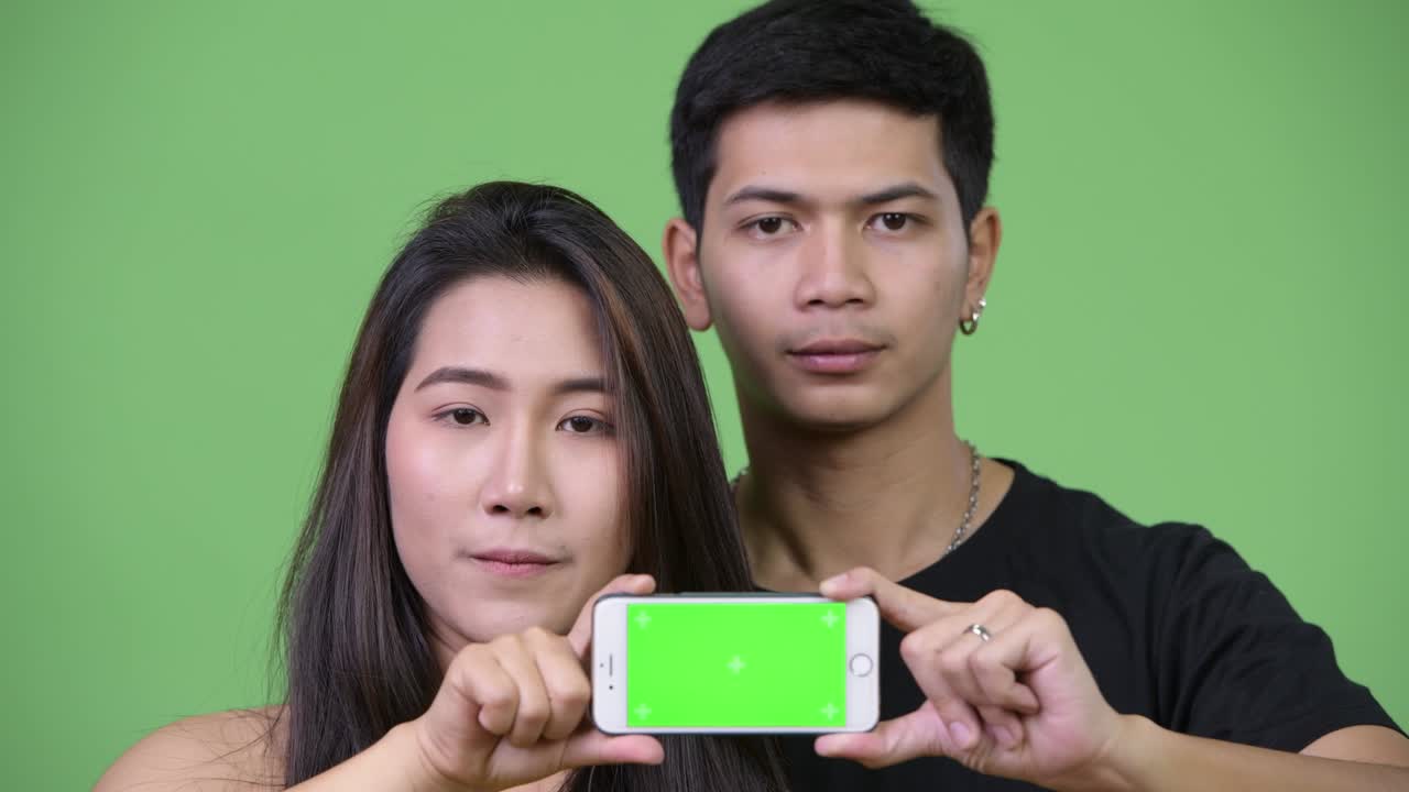 젊은 아시아 커플이 함께 전화를 보여주고 있습니다.
