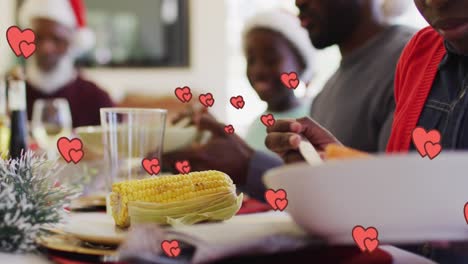 animación de corazones flotando sobre una feliz familia afroamericana durante la cena de navidad