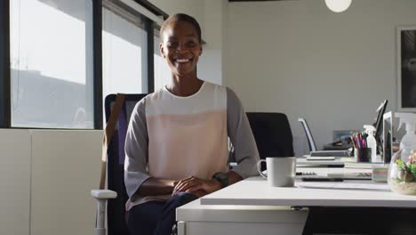 happy african american businesswoman sitting at desk and smiling at work