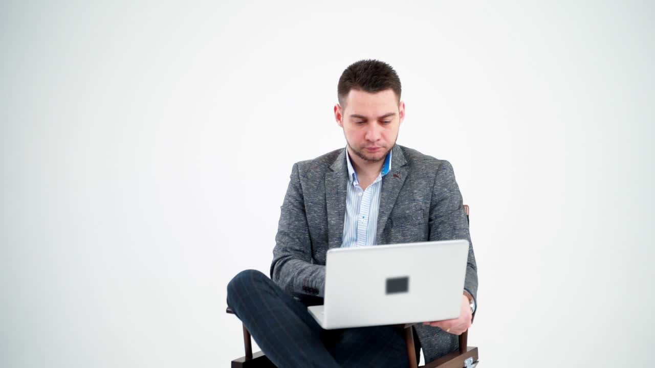 Thoughtful businessman sitting with a laptop. Handsome man in elegant clothing working on a modern laptop isolated on white background.