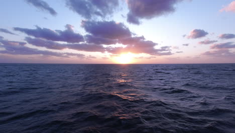 Toma-Panorámica-De-Una-Hermosa-Puesta-De-Sol-Sobre-El-Mar-Azul-Ondulado,-Cielo-Azul-Y-Nubes