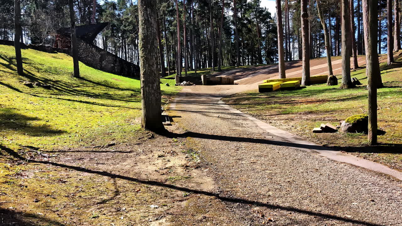 Forest path through park with sunlight and amphitheater in Jāņparks, Smiltene