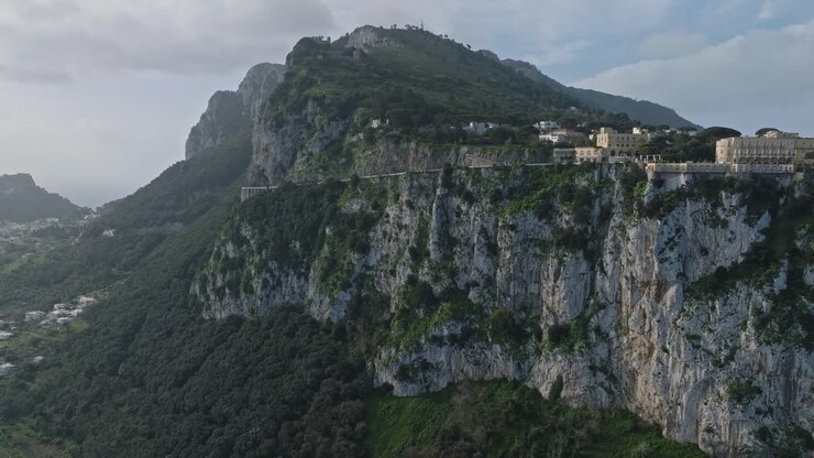Vista dalla scogliera di Capri con vegetazione lussureggiante e architettura storica, sotto un cielo sereno