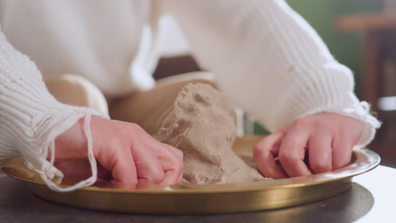 Lower view of mindful guest hands shaping soft mold into octopus figure on golden tray during calm therapy session, emphasizing focused engagement, tactile creativity, and stress relieving activity