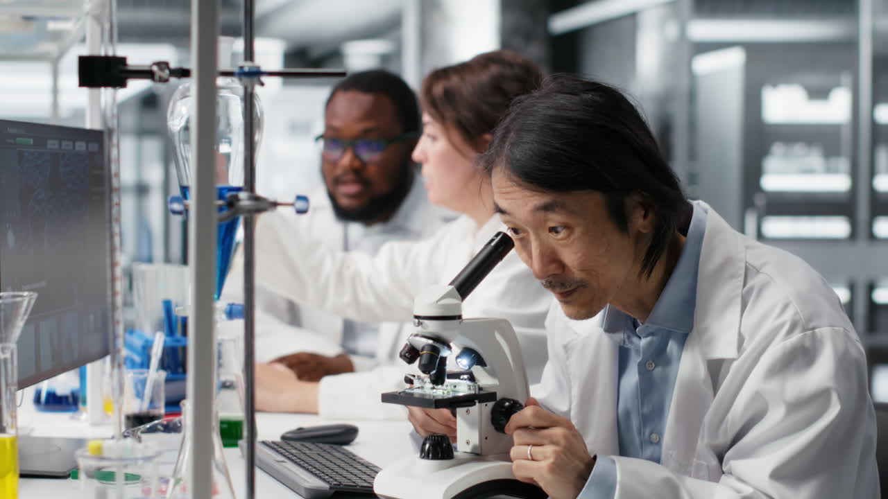 Vertical video Team leader writes down observations for lab coworkers using microscope