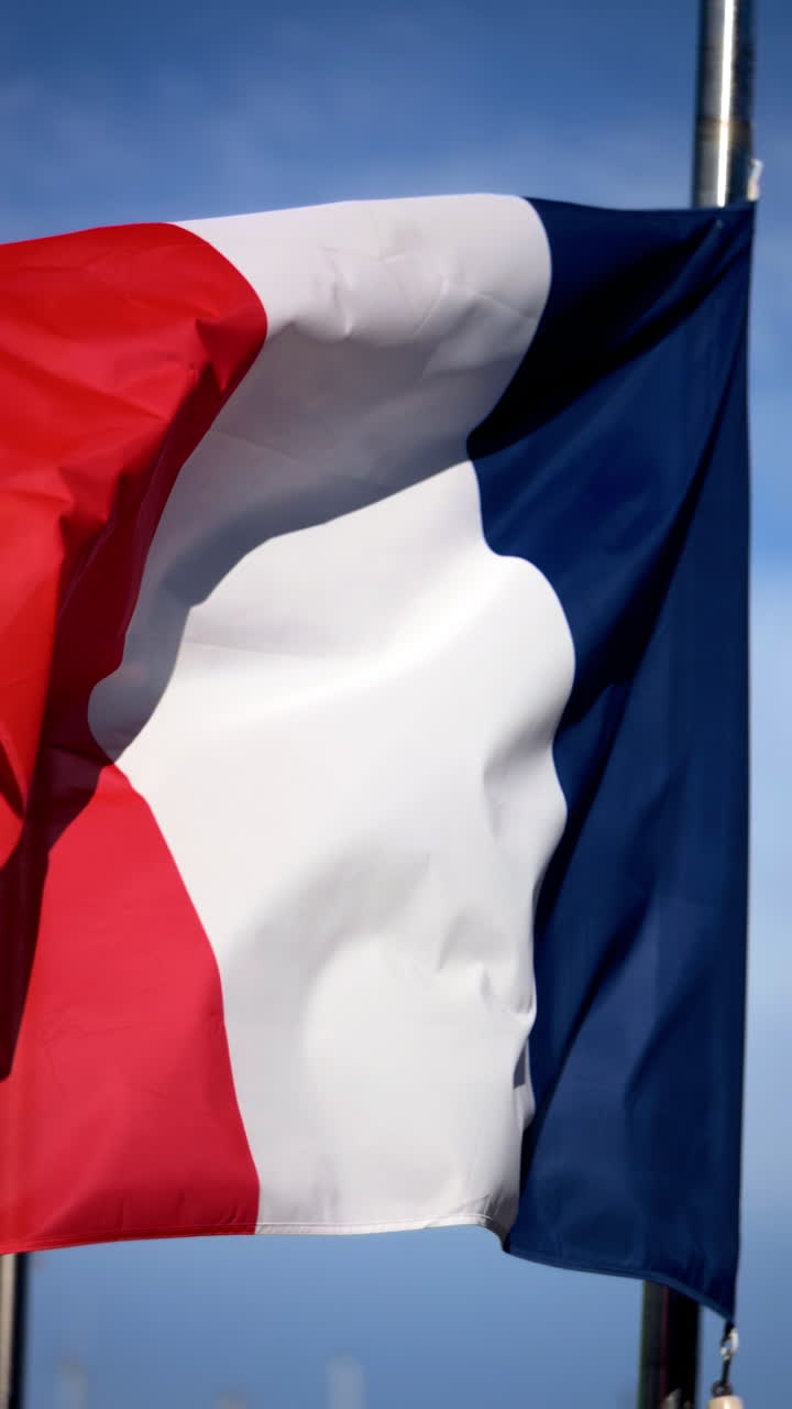 Primo piano della bandiera francese che sventola al vento con un cielo blu sullo sfondo. Verticale