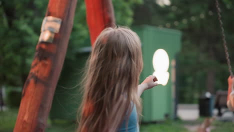 back view of young boy pushing friend on wooden chain swing in blurred park playground bathed in warm evening light capturing playful childhood moment among trees during summer dusk