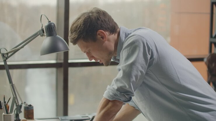 A man is a young modern architect sitting at a table drawing a plan of the building and developing a design sitting in an office in the Sitel loft near a large window. To create facades of buildings to design furniture and design the project of a residential complex.