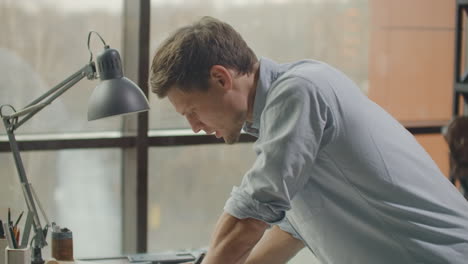 a man is a young modern architect sitting at a table drawing a plan of the building and developing a design sitting in an office in the sitel loft near a large window. to create facades of buildings to design furniture and design the project of a residential complex.