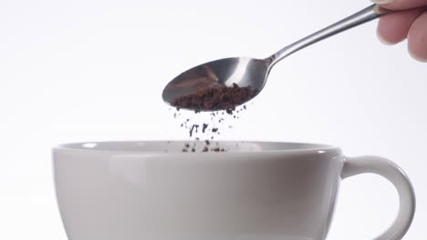 close up shot of pouring a instant coffee from spoon into coffee mug on white background