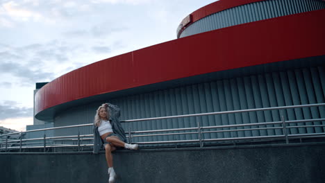 Sporty-girl-sitting-city-building-in-casual-clothes-at-evening-downtown.