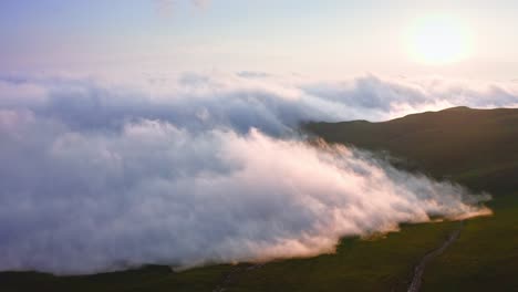 sunset in foggy mountains, dense clouds creeping over slanted plateau, aerial shot from drone