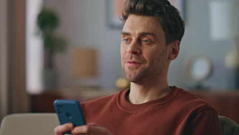positive guy texting mobile phone at home sofa close up. cheerful man messaging