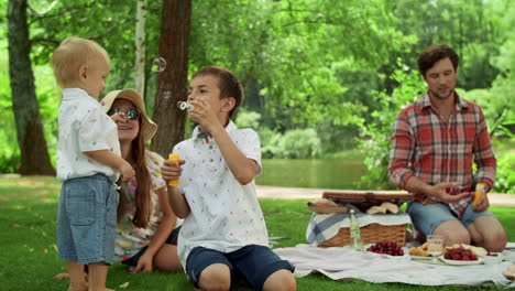 Children-having-fun-with-soap-bubbles-in-park.-Parents-talking-together-outdoors