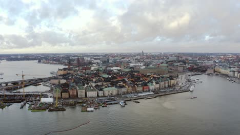 Old-town-of-Stockholm,-Gamla-Stan-Island-and-reconstruction-site-with-cranes-near-bridge,-cloudy-late-afternoon