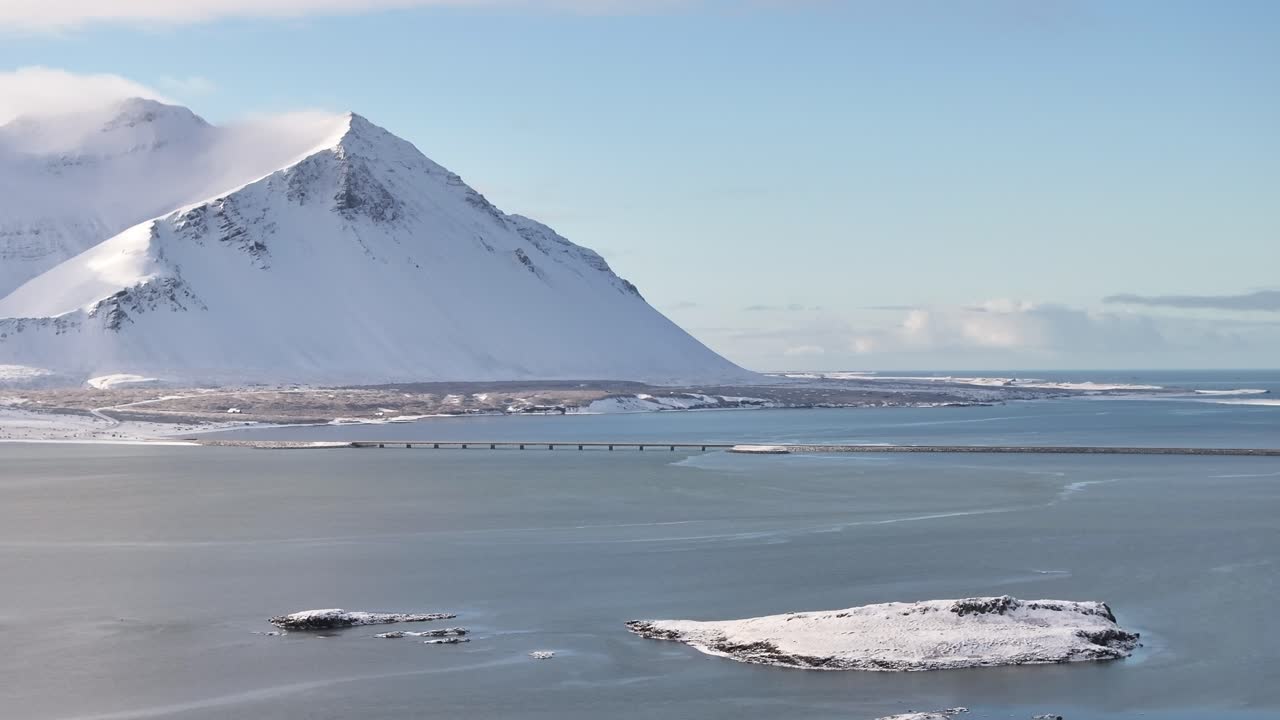 Beautiful drone view of snow-covered mountains, frozen lake and bridge near Borgarnes, Iceland, drone slowly pushes in.