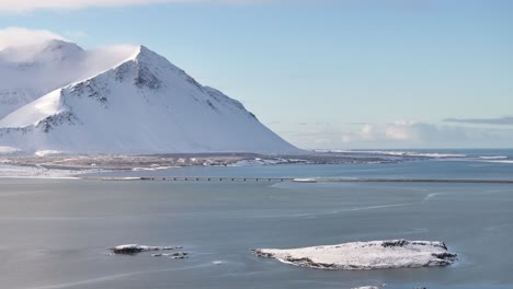 beautiful drone view of snow-covered mountains, frozen lake and bridge near borgarnes, iceland, drone slowly pushes in.