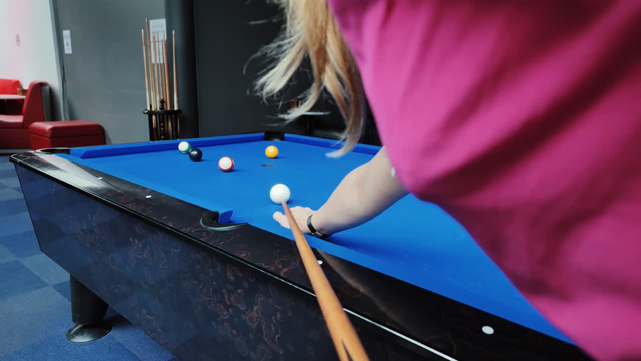 Slowmotionopname van vrouw in roze shirt die een nauwkeurige poolstoot uitvoert in een lichte ruimte