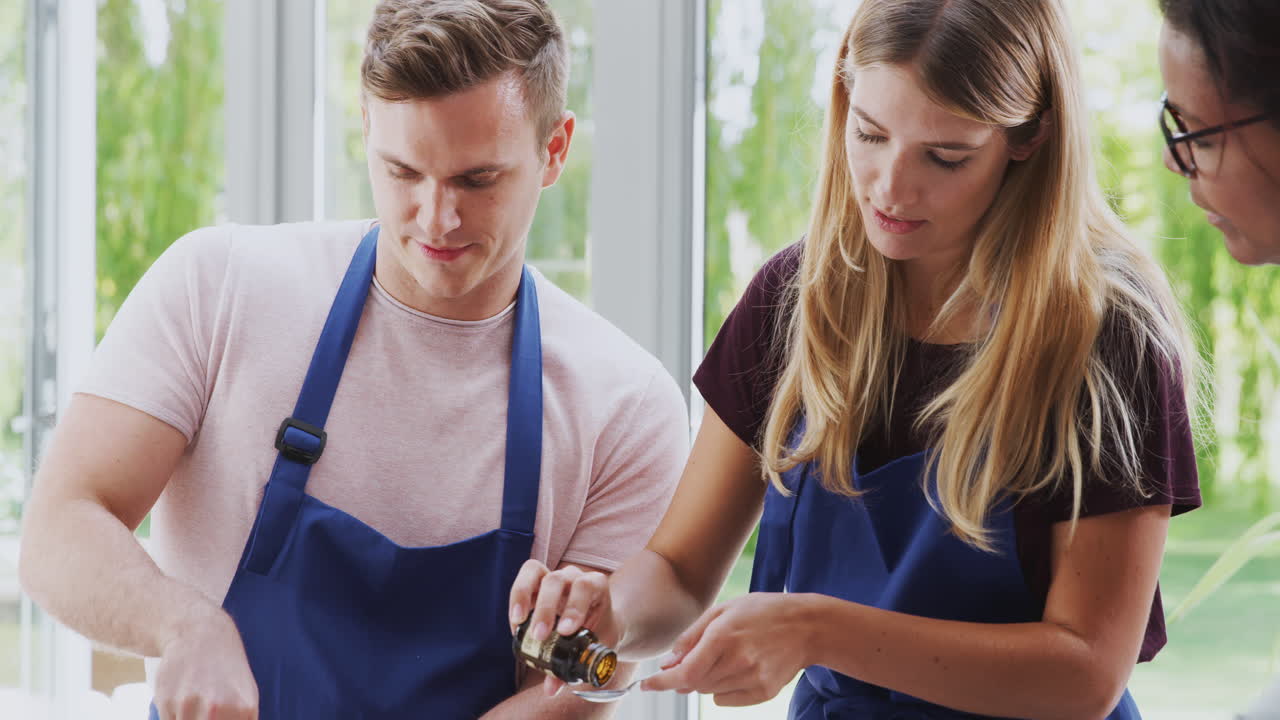 Male And Female Adult Students Measuring Ingredients In Cookery Class In Kitchen