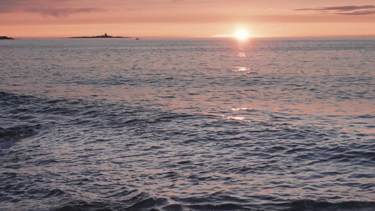 가라앉는 태양의 따뜻한 빛에 빛나는 파도가 천천히 바위가 있는 해변을 향해