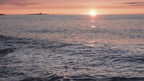 olas iluminadas por el cálido resplandor del sol poniente oll lentamente en la orilla rocosa