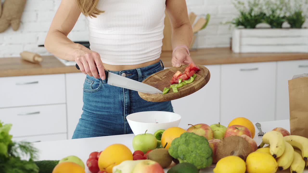 The girl mixes in a plate pepper and red tomato. Cooking a salad of fruits and vegetables