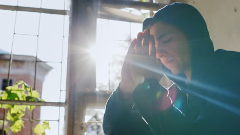 a young man in a hood sitting on a window praying or very thoughtful in the rays of the sun